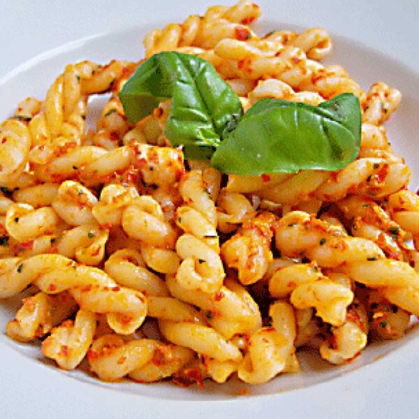A plate of twisted pasta in a tomato-based sauce, garnished with two fresh basil leaves, served on a white dish.