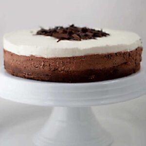 A two-layer chocolate mousse cake with a dark chocolate base and a creamy white top, garnished with chocolate shavings, displayed on a white cake stand.