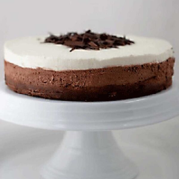 A two-layer chocolate mousse cake with a dark chocolate base and a creamy white top, garnished with chocolate shavings, displayed on a white cake stand.