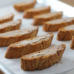 Rows of golden brown biscotti slices are arranged on a parchment-lined baking sheet, ready for serving or cooling.