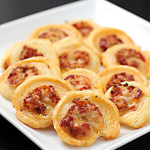 A white plate holds several golden-brown puff pastry pinwheels filled with a savory mixture, arranged neatly on a dark surface.