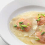 Three round ravioli served in a shallow white bowl with a light broth, garnished with chopped green onions.