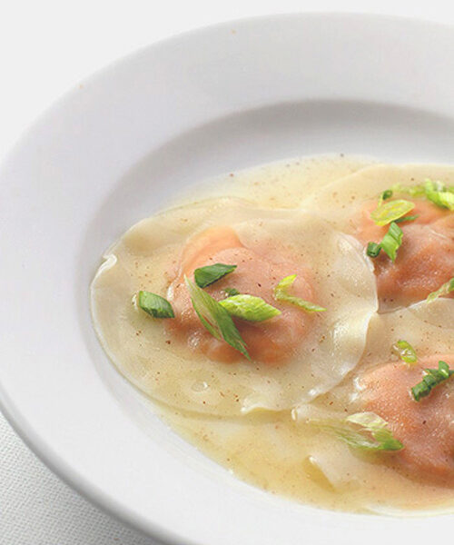 Three round ravioli served in a shallow white bowl with a light broth, garnished with chopped green onions.