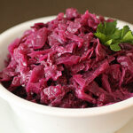 A white bowl filled with cooked red cabbage, garnished with a sprig of fresh parsley, sits on a matching white saucer.