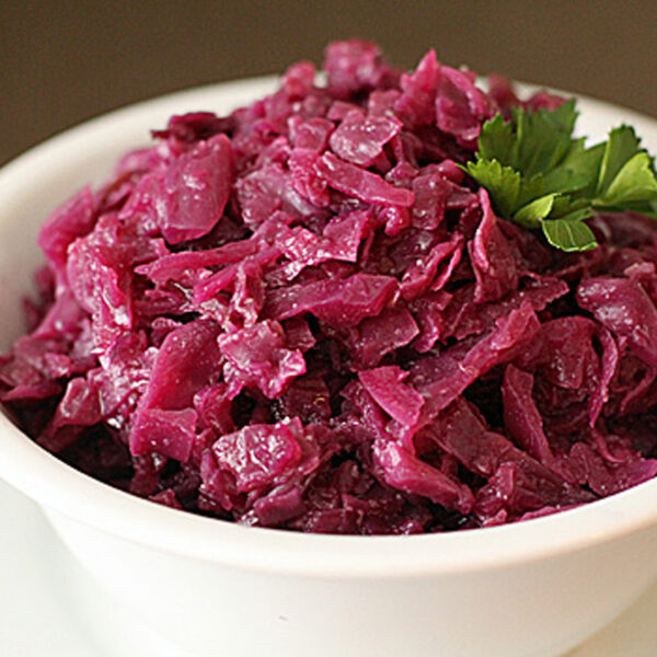 A white bowl filled with cooked red cabbage, garnished with a sprig of fresh parsley, sits on a matching white saucer.