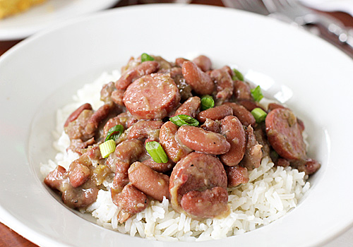 A white bowl filled with white rice topped with red beans, sliced sausage, and garnished with chopped green onions.