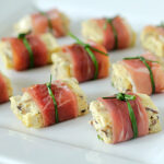 Small appetizers featuring pieces of savory egg omelette with herbs, wrapped in prosciutto and tied with green chive on a white rectangular plate.