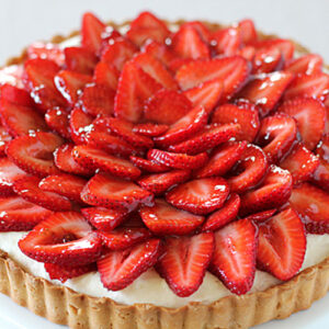 A strawberry tart with a golden crust, filled with cream and topped with neatly arranged slices of fresh, glossy strawberries.