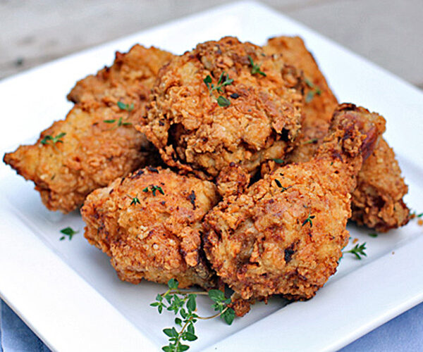 A square white plate filled with several pieces of golden-brown fried chicken, garnished with small sprigs of fresh herbs.