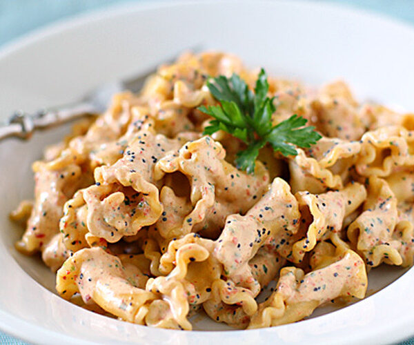 A plate of mafaldine pasta coated in a creamy sauce, garnished with fresh parsley and sprinkled with black pepper, with a fork resting on the side.