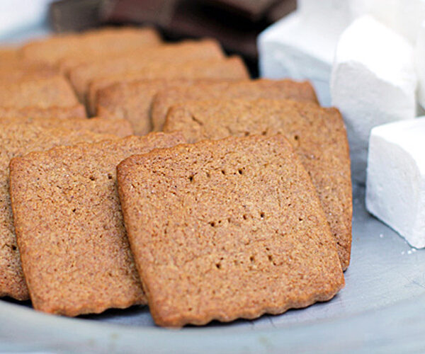 Square graham crackers are arranged on a plate next to a stack of fluffy white marshmallows and pieces of chocolate, ready for making smores.