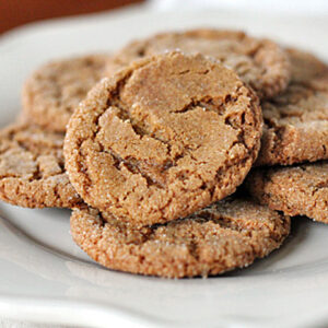 A plate filled with several golden-brown, sugar-coated cookies stacked on top of each other, displayed on a white dish.