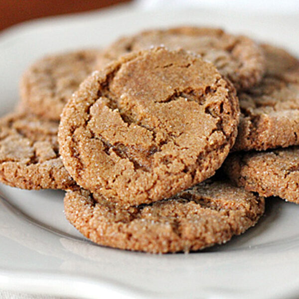 A plate filled with several golden-brown, sugar-coated cookies stacked on top of each other, displayed on a white dish.