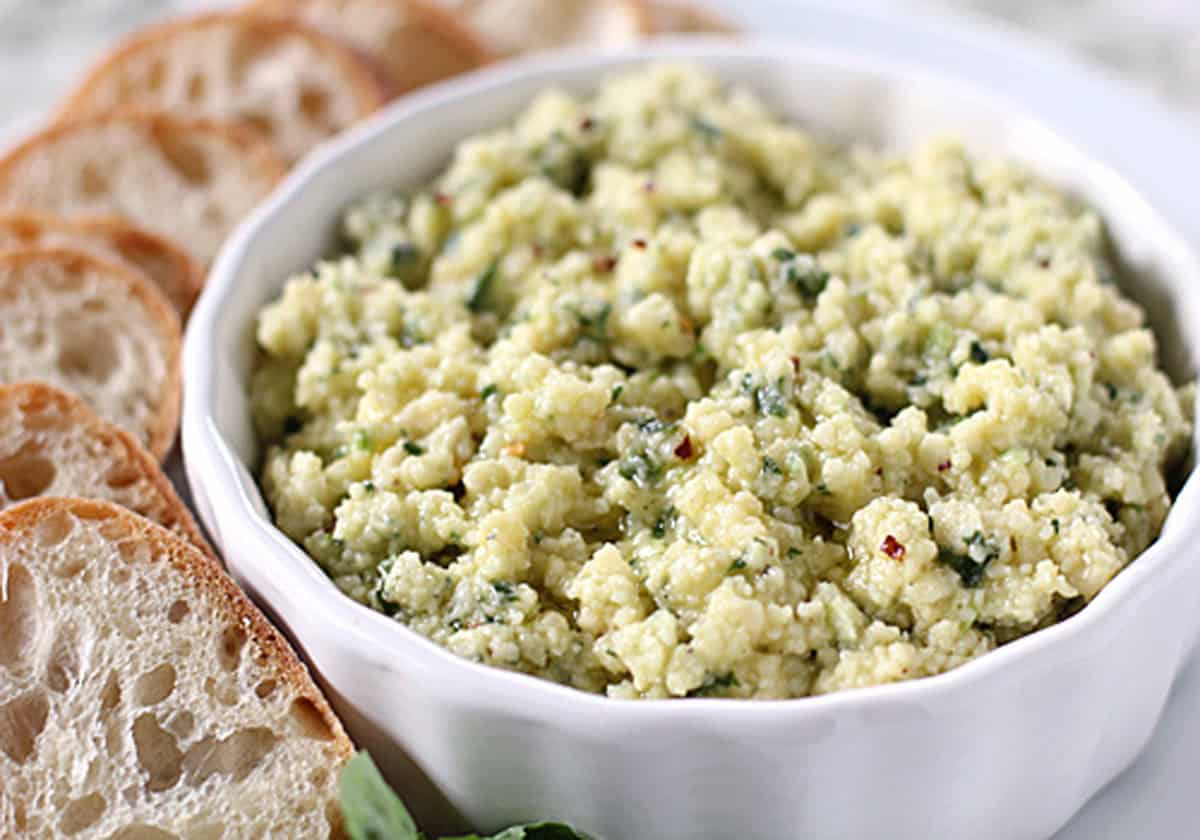 A white bowl filled with herbed ricotta cheese, surrounded by several slices of crusty bread on a plate.