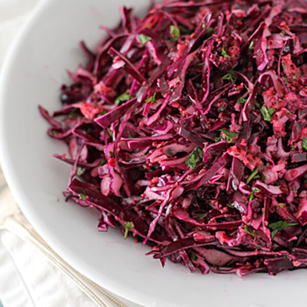 A white bowl filled with shredded red cabbage salad mixed with herbs, placed on a white napkin with a fork beside it.