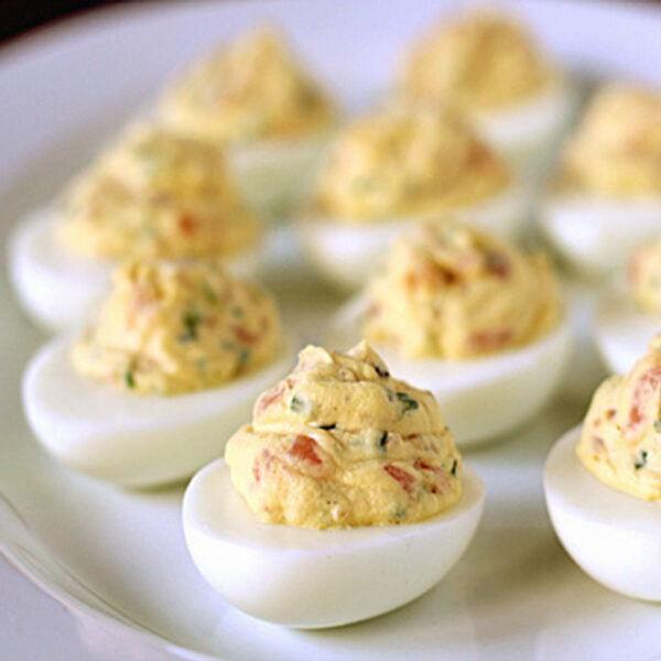 A white plate filled with several deviled eggs, each halved and topped with a creamy, yellow, seasoned filling containing visible herbs.