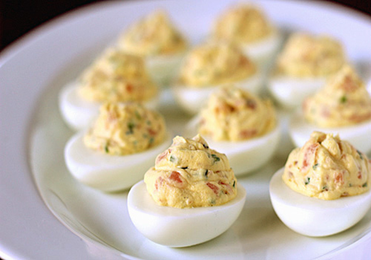 A white plate filled with several deviled eggs, each halved and topped with a creamy, yellow, seasoned filling containing visible herbs.