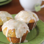 Three glazed muffins with poppy seeds on a green plate, with a white teacup filled with tea in the background.