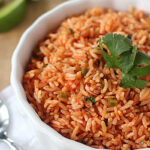 A bowl of Mexican rice garnished with cilantro, with lime wedges and a spoon on a white napkin nearby.