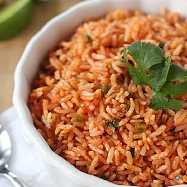 A bowl of Mexican rice garnished with cilantro, with lime wedges and a spoon on a white napkin nearby.