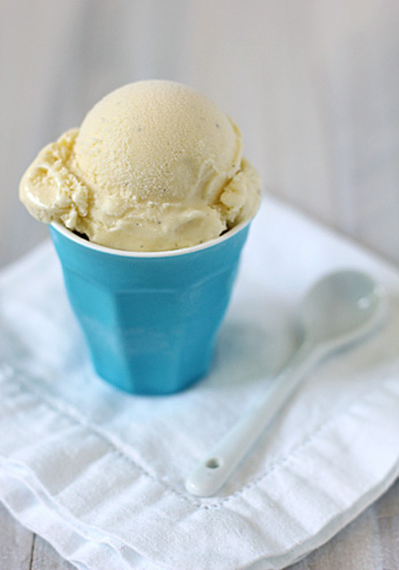 A scoop of vanilla ice cream in a blue cup sits on a folded white cloth napkin, with a white spoon placed beside it.