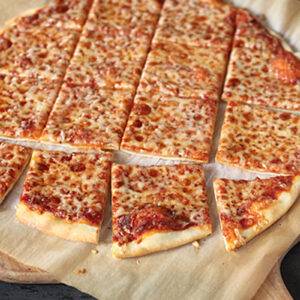 A cheese pizza on parchment paper, cut into rectangular strips and squares, resting on a wooden surface.