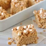 A close-up of Fluffer-nutter Treats—peanut butter Rice Krispies treats topped with mini marshmallows and a drizzle of peanut butter, with more treats in a white dish behind.