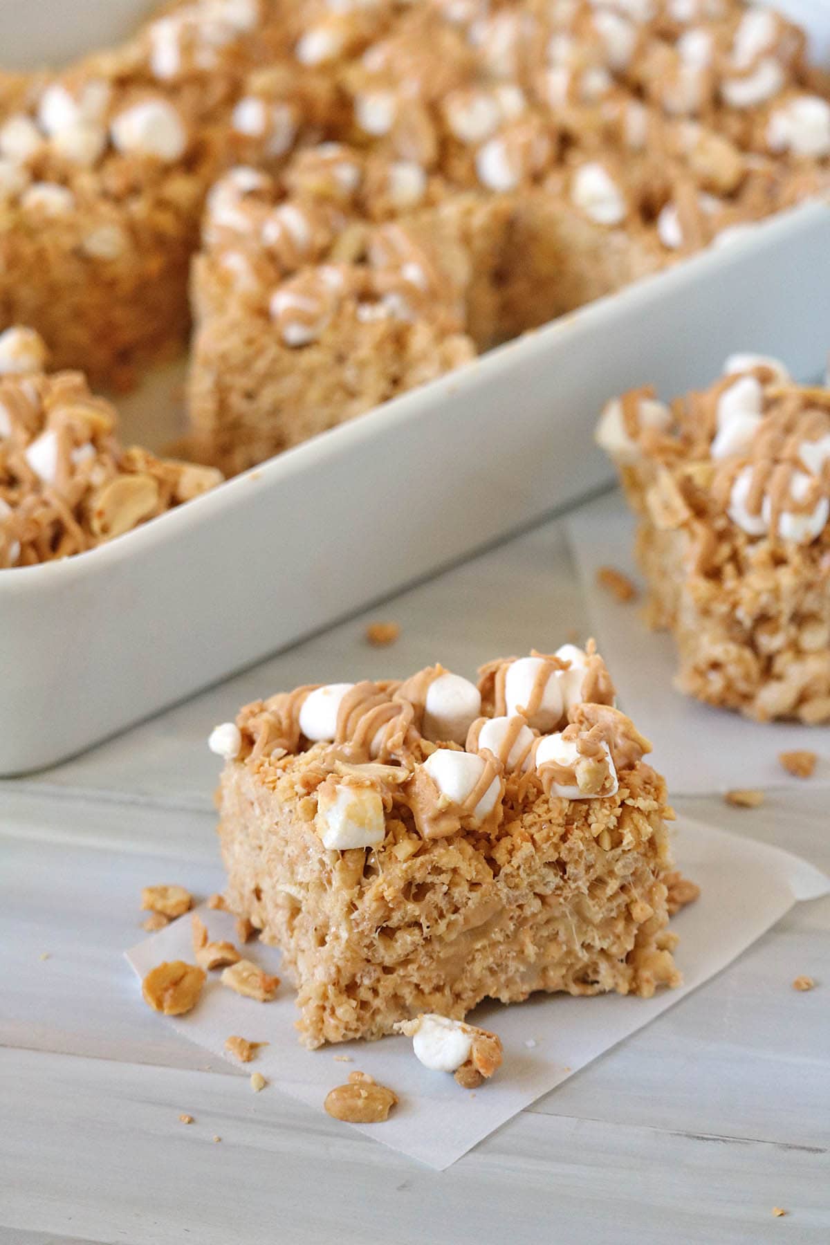 A close-up of Fluffer-nutter Treats&mdash;peanut butter Rice Krispies treats topped with mini marshmallows and a drizzle of peanut butter, with more treats in a white dish behind.