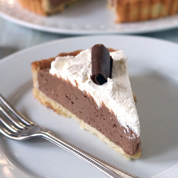 A slice of chocolate cream pie topped with whipped cream and a chocolate curl, served on a white plate with a fork.
