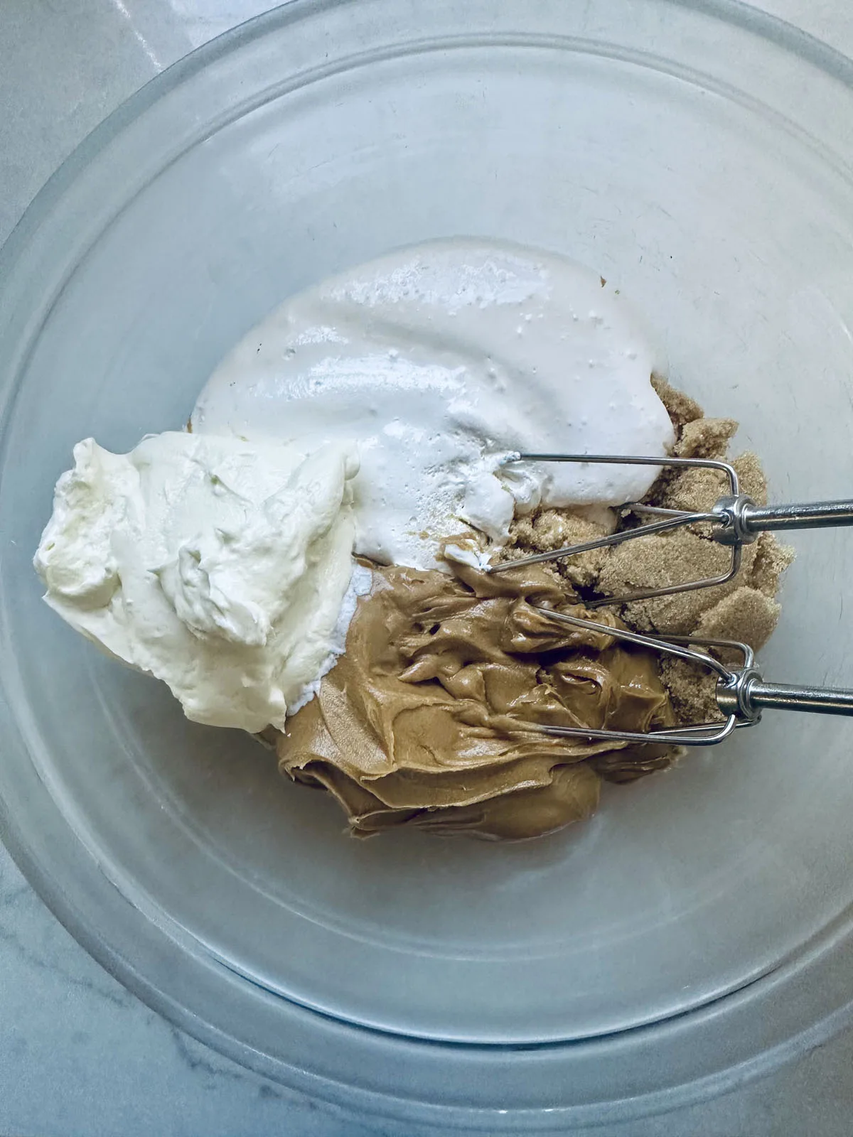 A mixing bowl containing ingredients for a peanut butter chocolate tart—peanut butter, whipped cream, marshmallow fluff, and brown sugar—with a hand mixer resting inside.
