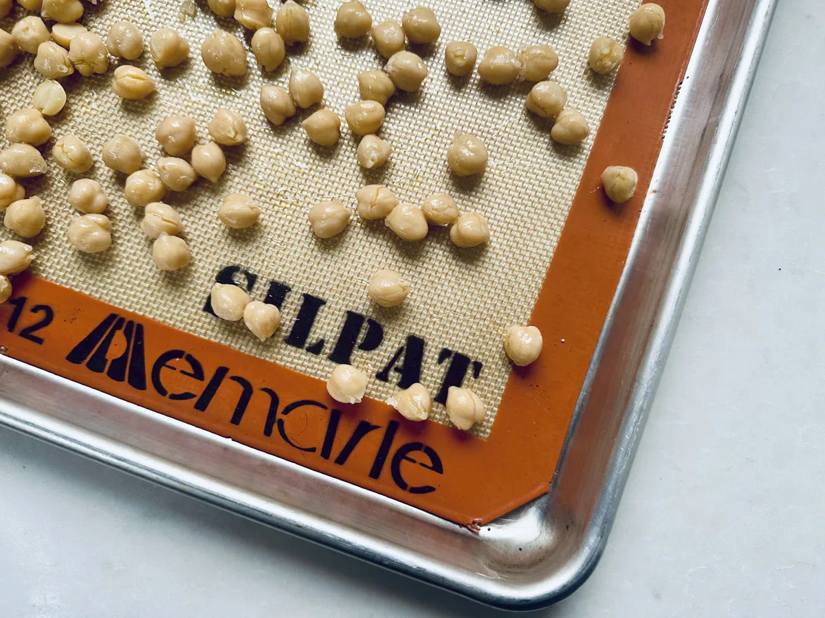 Chickpeas are spread on a SILPAT and Memarle silicone baking mat atop a metal sheet, ready to become the perfect roasted chickpeas snack as part of your favorite roasted chickpeas recipe.