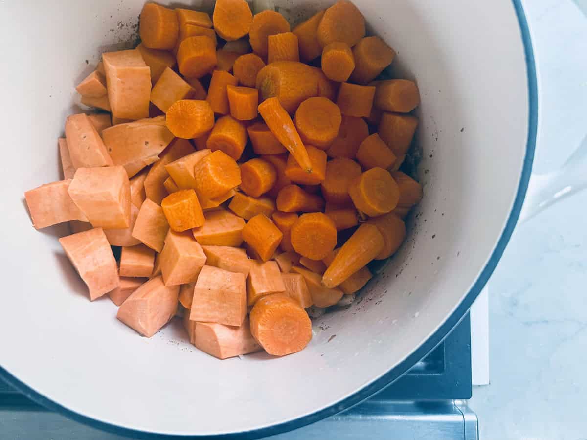 Diced carrots and sweet potatoes in a white pot on a stove, ready to be cooked.