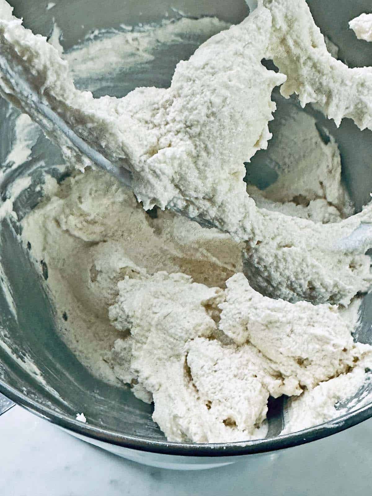A close-up of thick, creamy batter being mixed in a metal bowl with a stand mixer attachment, showing a smooth, fluffy texture.