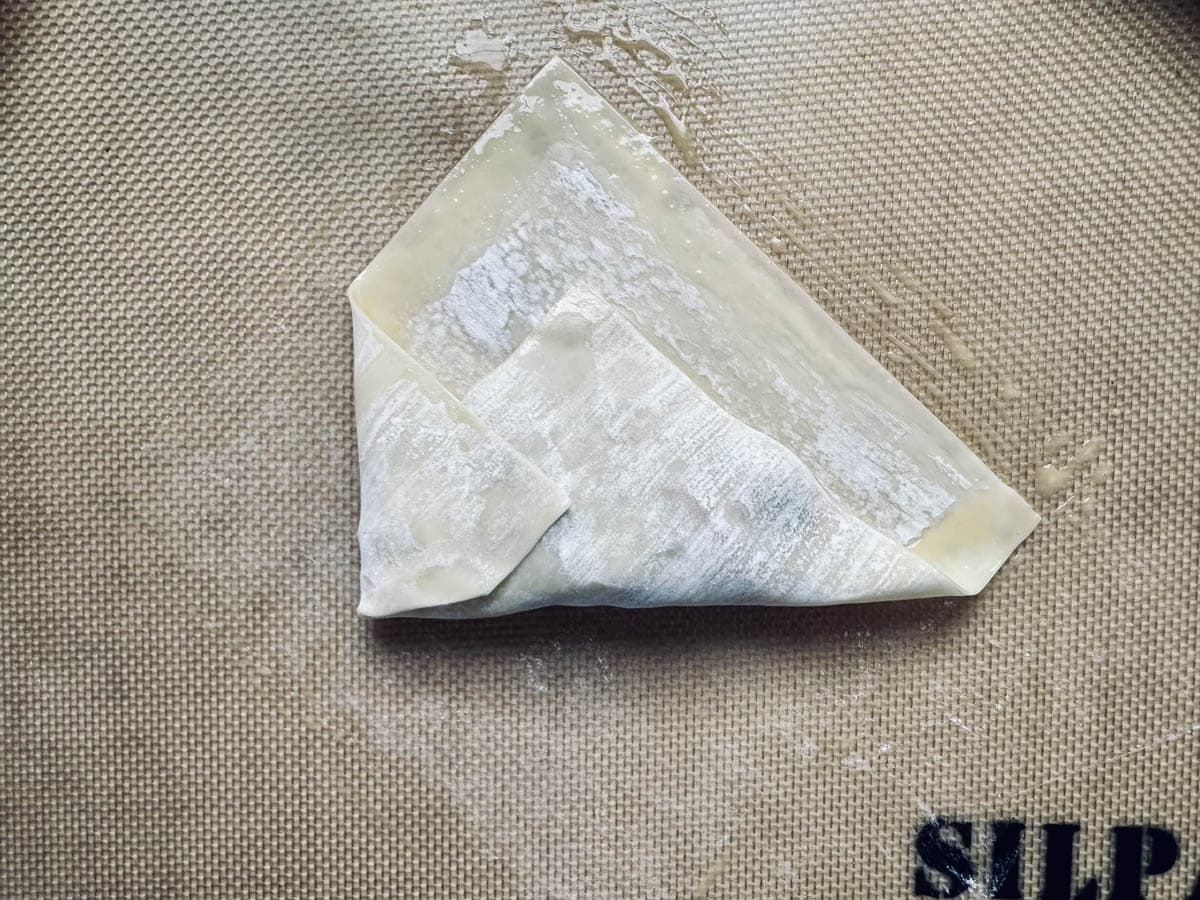 A single folded wonton wrapper sits on a textured silicone baking mat, with the letters SILP partially visible in the bottom right corner.