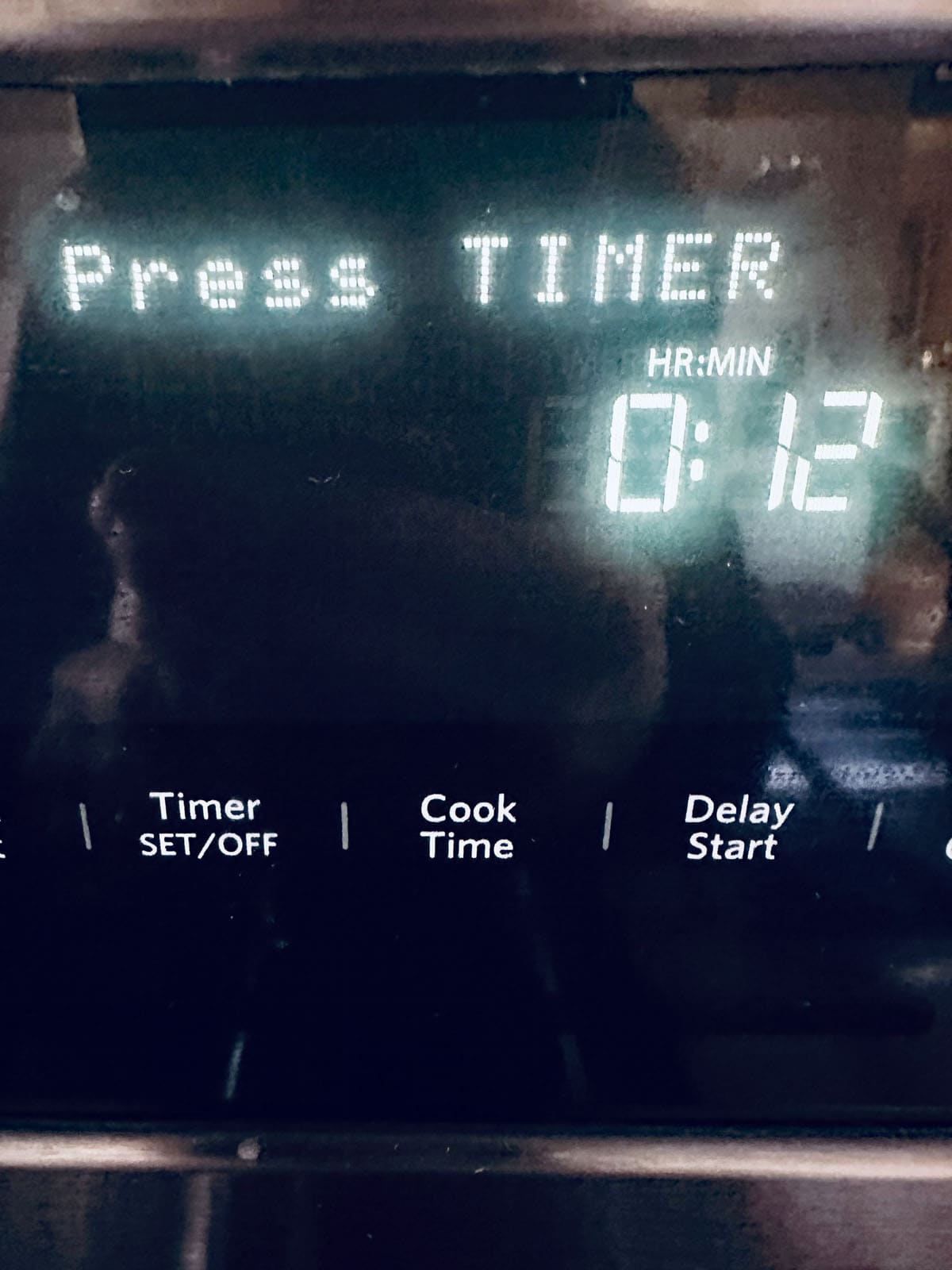 A close-up of an oven control panel displays Press TIMER on the screen, with 0:12 minutes remaining. Buttons for Timer, Cook Time, and Delay Start are visible below the display.