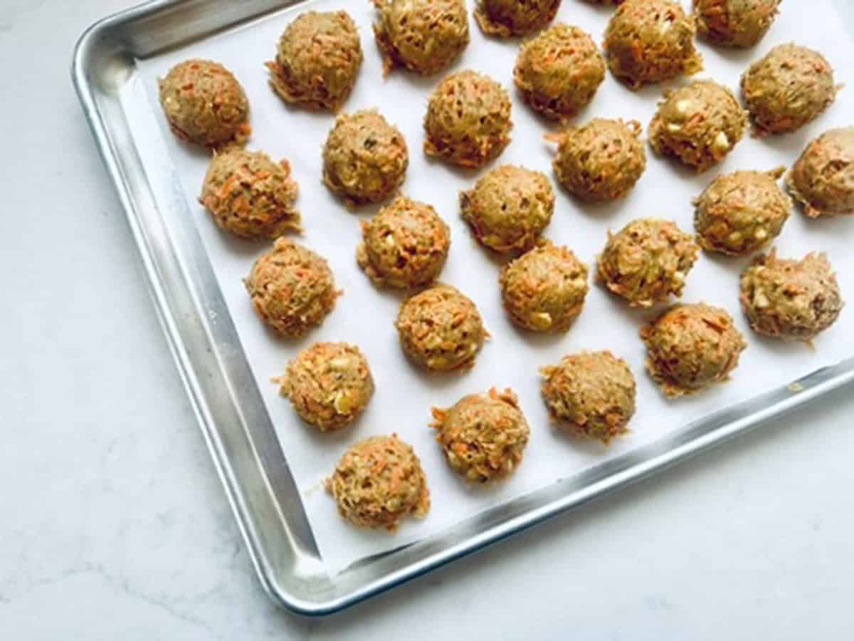 A baking sheet lined with parchment paper displays rows of evenly spaced, raw cookie dough balls, ready to be baked.