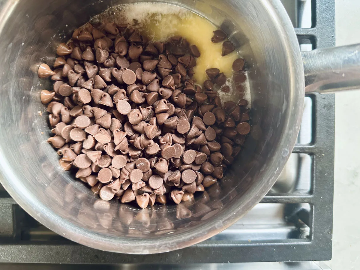 A saucepan with chocolate chips and melted butter inside, placed on a stovetop, ready to be melted together.