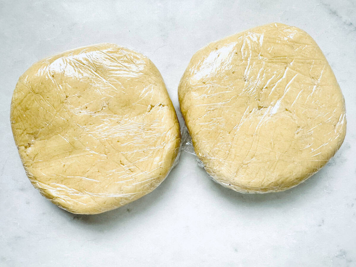 Two discs of dough for Strawberry Shortcake Cookies are wrapped in plastic wrap and placed side by side on a light-colored surface.