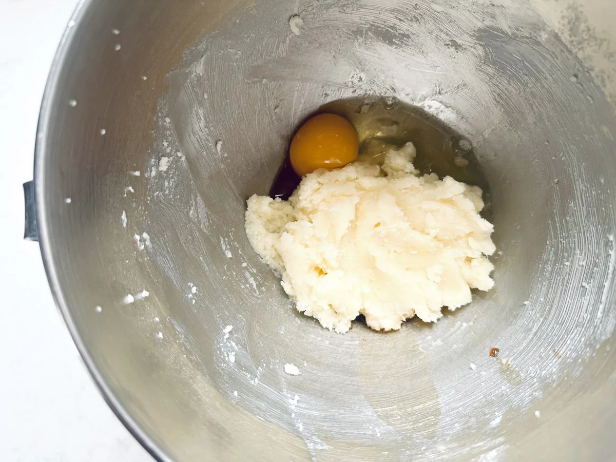 A metal mixing bowl containing a mound of creamed butter and sugar with a single raw egg cracked on top, ready to be mixed together for delicious Strawberry Shortcake Cookies.