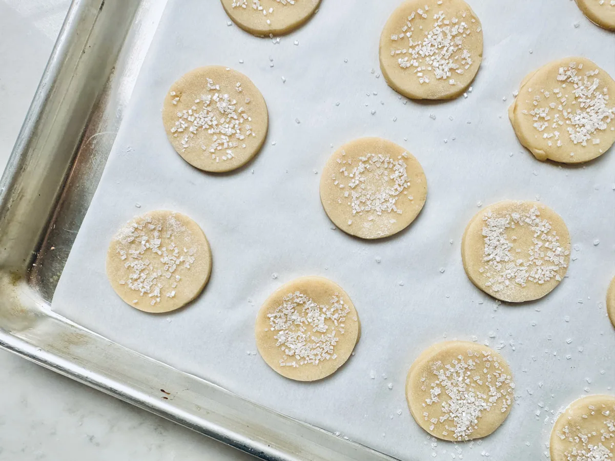 Unbaked round Strawberry Shortcake Cookies sprinkled with coarse sugar are arranged on a parchment-lined baking sheet, ready to go into the oven.