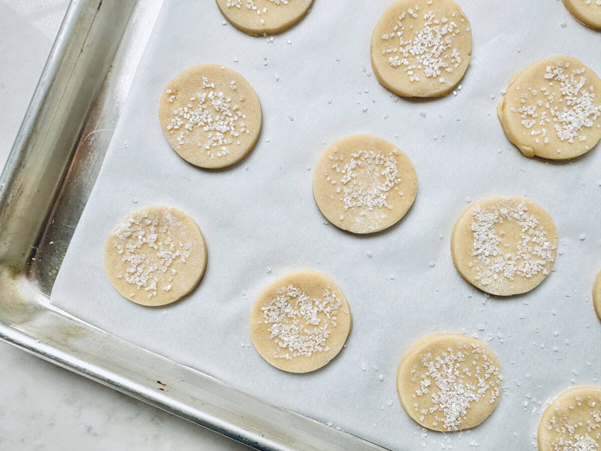 Unbaked round Strawberry Shortcake Cookies sprinkled with coarse sugar are arranged on a parchment-lined baking sheet, ready to go into the oven.