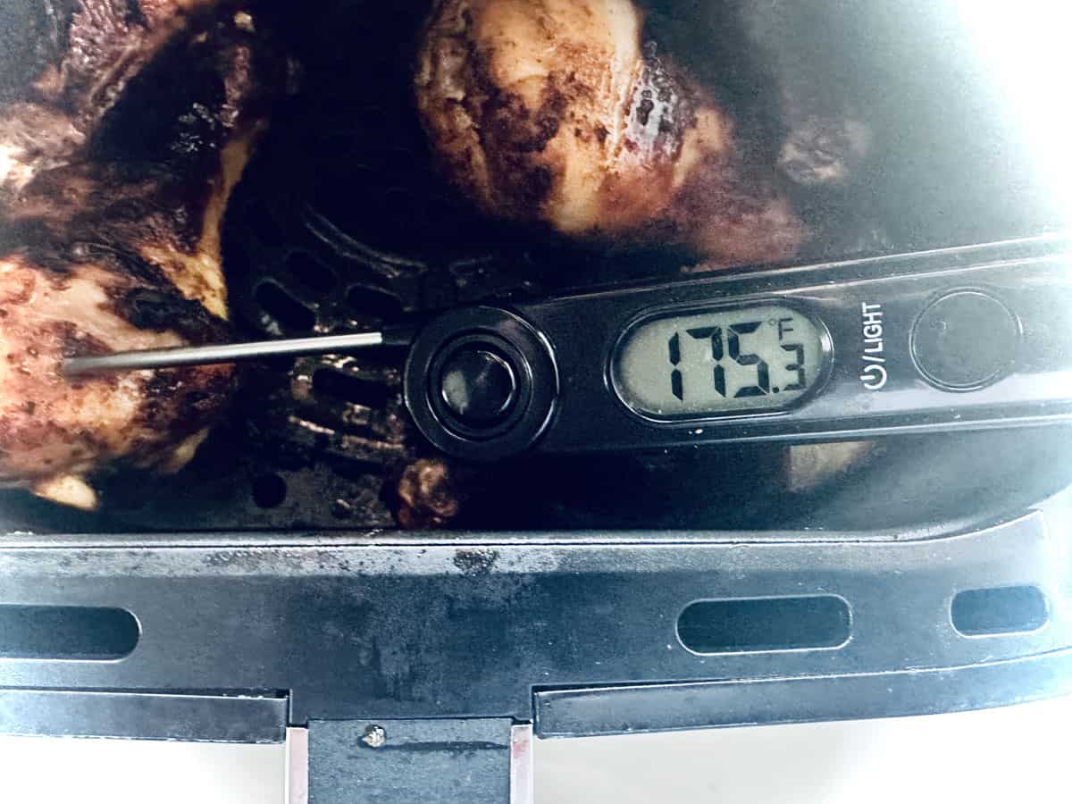 A close-up of a digital meat thermometer reading 175.3°F inserted into pieces of Air-Fried Peruvian Chicken with Green Crema inside an air fryer basket.