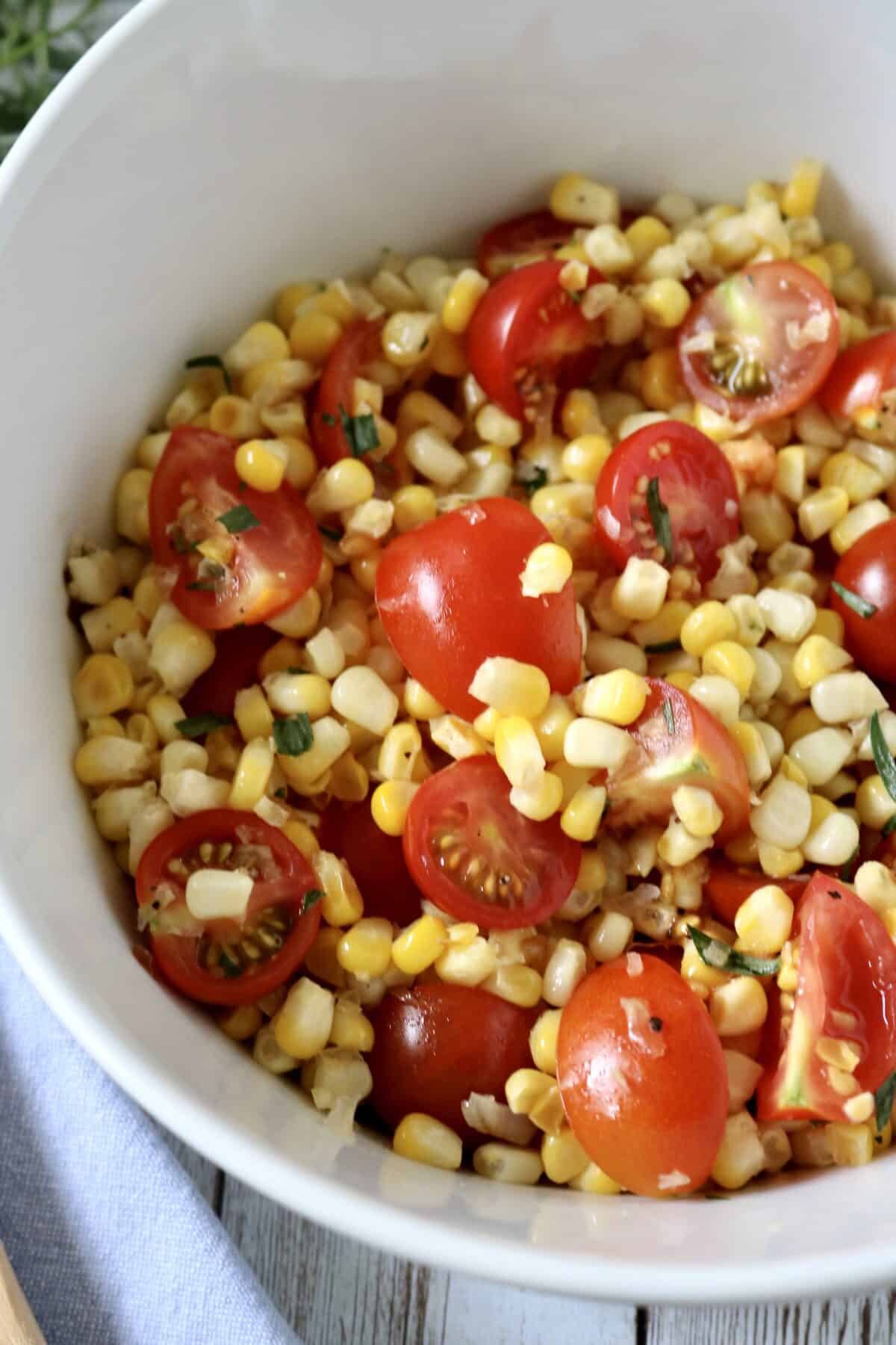 A white bowl filled with a fresh salad made of corn kernels, halved cherry tomatoes, and chopped herbs.