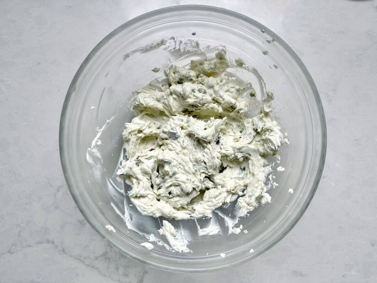 Glass bowl with herbed cream cheese mixture on a light marble surface; flecks of green herbs and seasoning are visible throughout the creamy, spreadable mixture—just like Vivian Howard’s Party Magnet, it’s irresistibly inviting and perfect for any gathering.