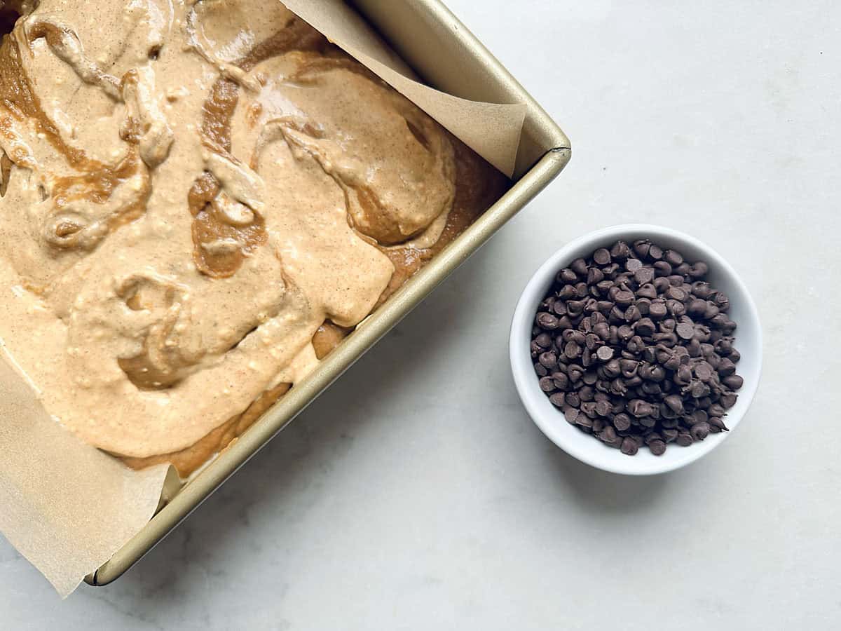 A square baking pan containing swirled batter next to a small bowl filled with chocolate chips.
