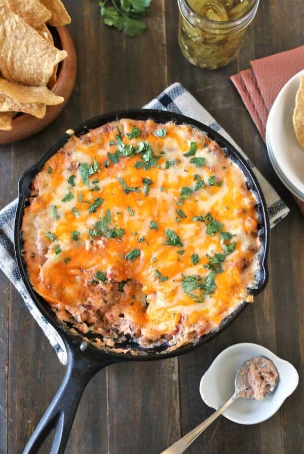 Baked black-eyed pea dip in a cast iron skillet topped with cilantro, served with a side of tortilla chips and pickled jalapeños.
