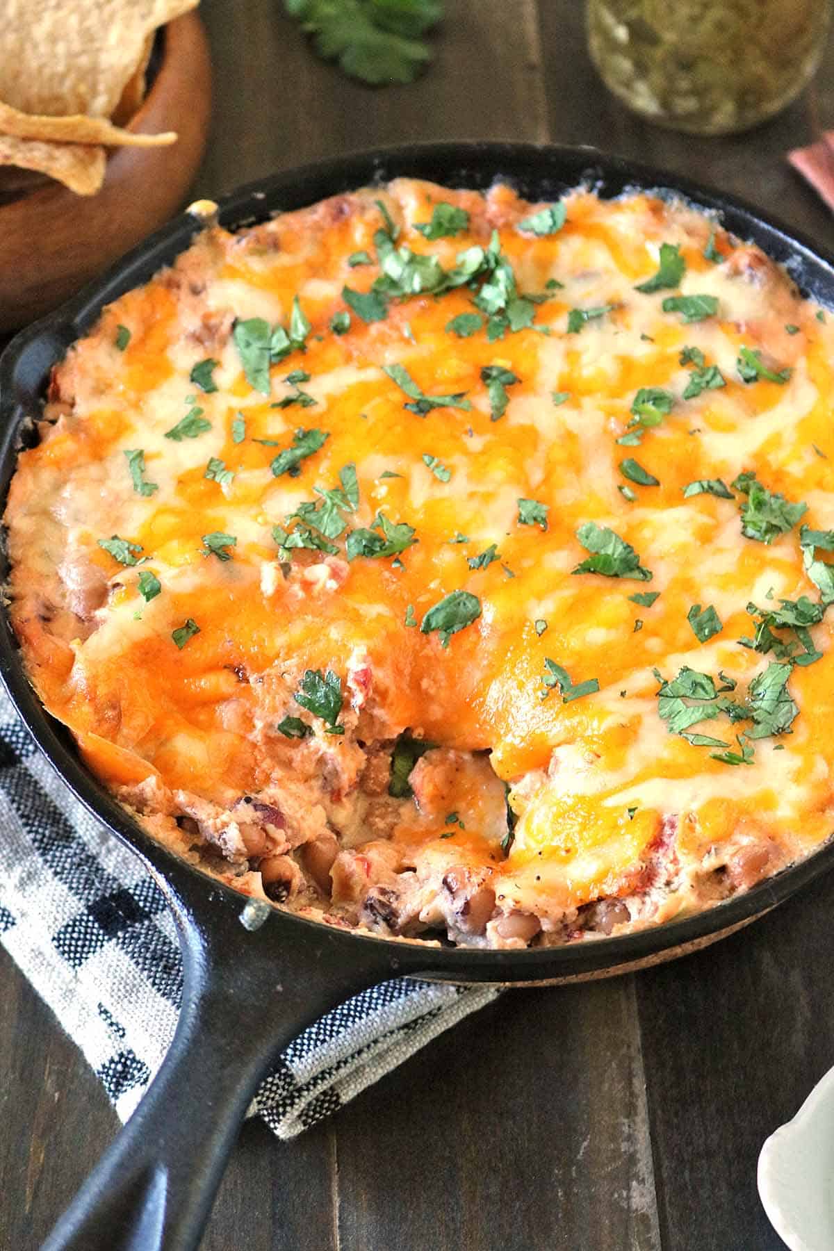 Cast-iron skillet filled with baked black-eyed pea dip topped with melted cheese and fresh cilantro.