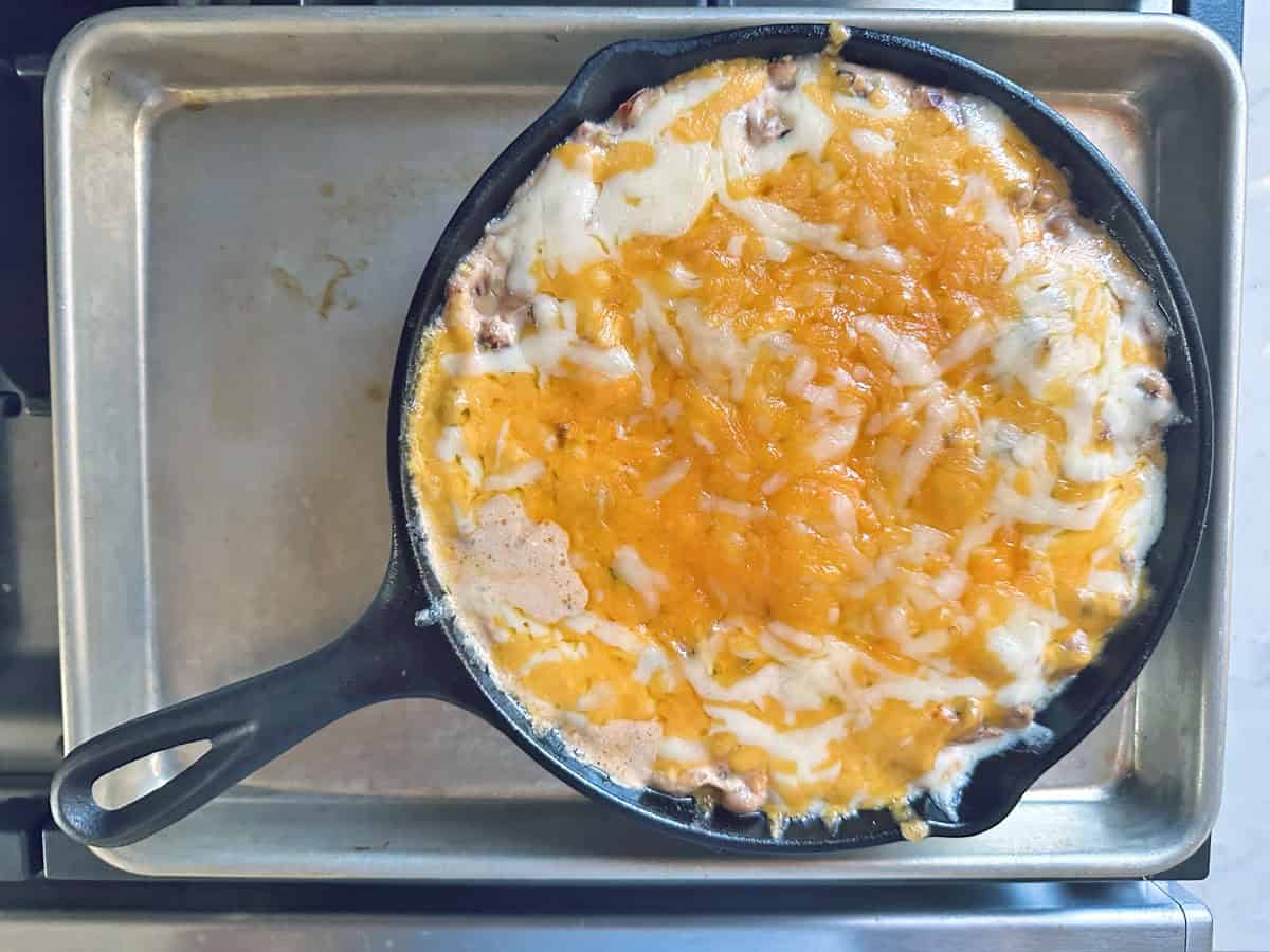 A cast iron skillet filled with baked black-eyed pea dip topped with melted shredded cheese, sitting on a metal baking sheet.
