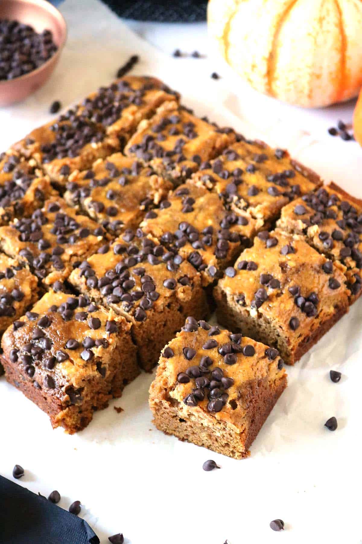 A tray of square pumpkin chocolate chip bars, with one piece pulled forward.